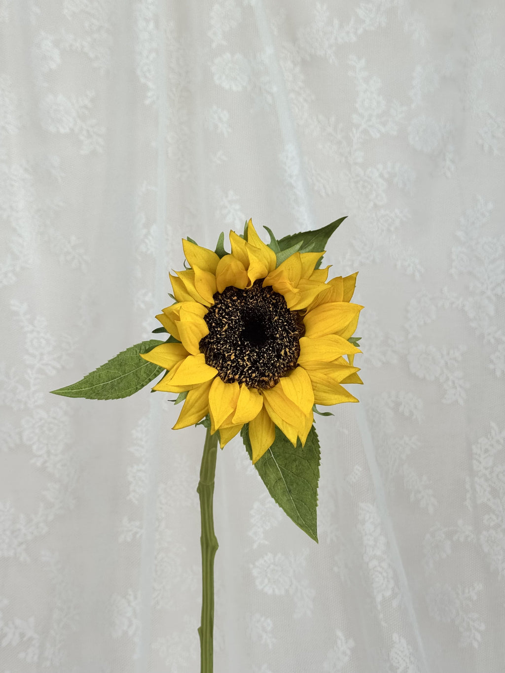 Close-up of a Fleuristic artificial sunflower showing vibrant yellow petals and detailed green foliage.